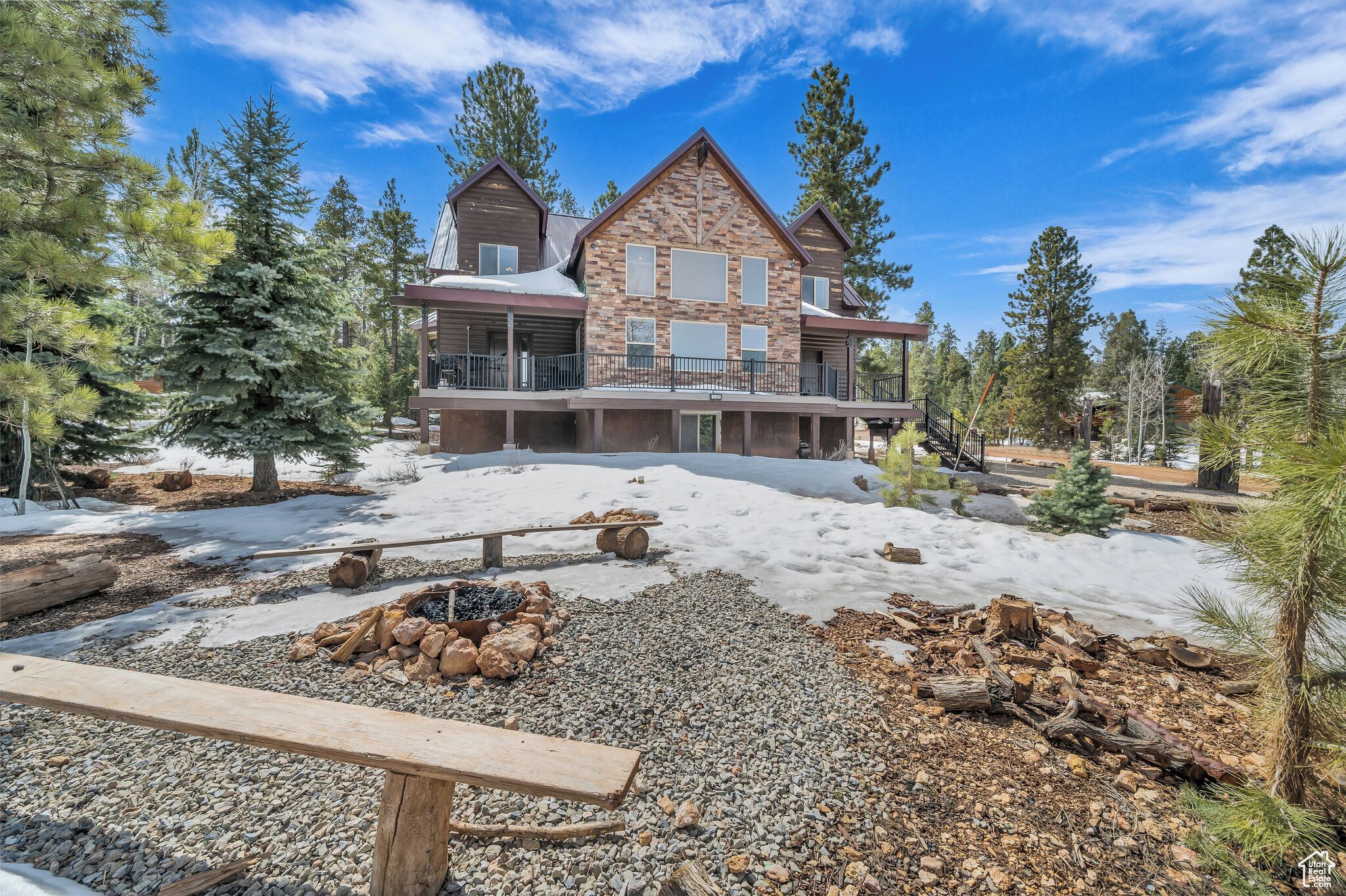 Un chalet à deux étages avec une façade en pierre, une terrasse couverte et un espace aménagé avec un foyer.