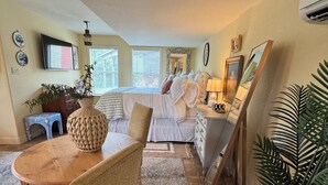 A cozy room with a bed, a dining table with chairs, a TV, and a large mirror.