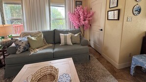 A cozy living room with a grey sofa, a wooden coffee table, and a pink artificial tree.
