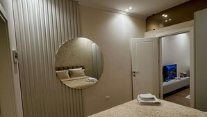A hotel room with a bed, a round mirror, a television, and a small seating area with a table and chairs. - Eliz Stay: Your Cozy Home Away From Home, Steps from the Lake. (Tiranë)