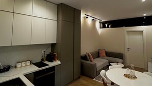 A modern kitchen with a dining area, a sofa, and a door. - Eliz Stay: Your Cozy Home Away From Home, Steps from the Lake. (Tiranë)