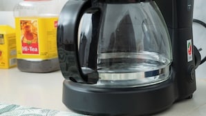 A black coffee maker with a clear glass carafe on a kitchen counter.