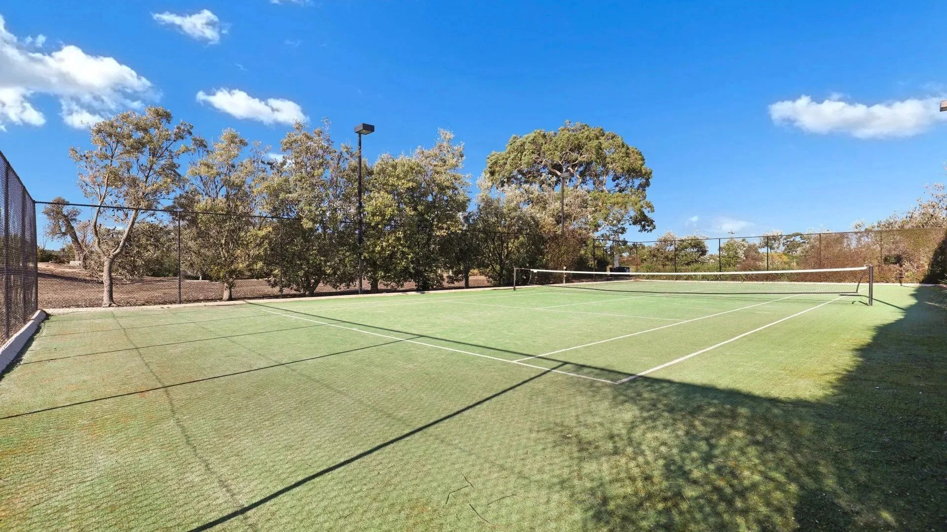An outdoor tennis court with a net, surrounded by trees and a clear sky.