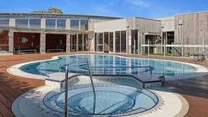 Una piscina moderna con cubierta de madera, puertas de cristal y un edificio con fachada de madera al fondo.