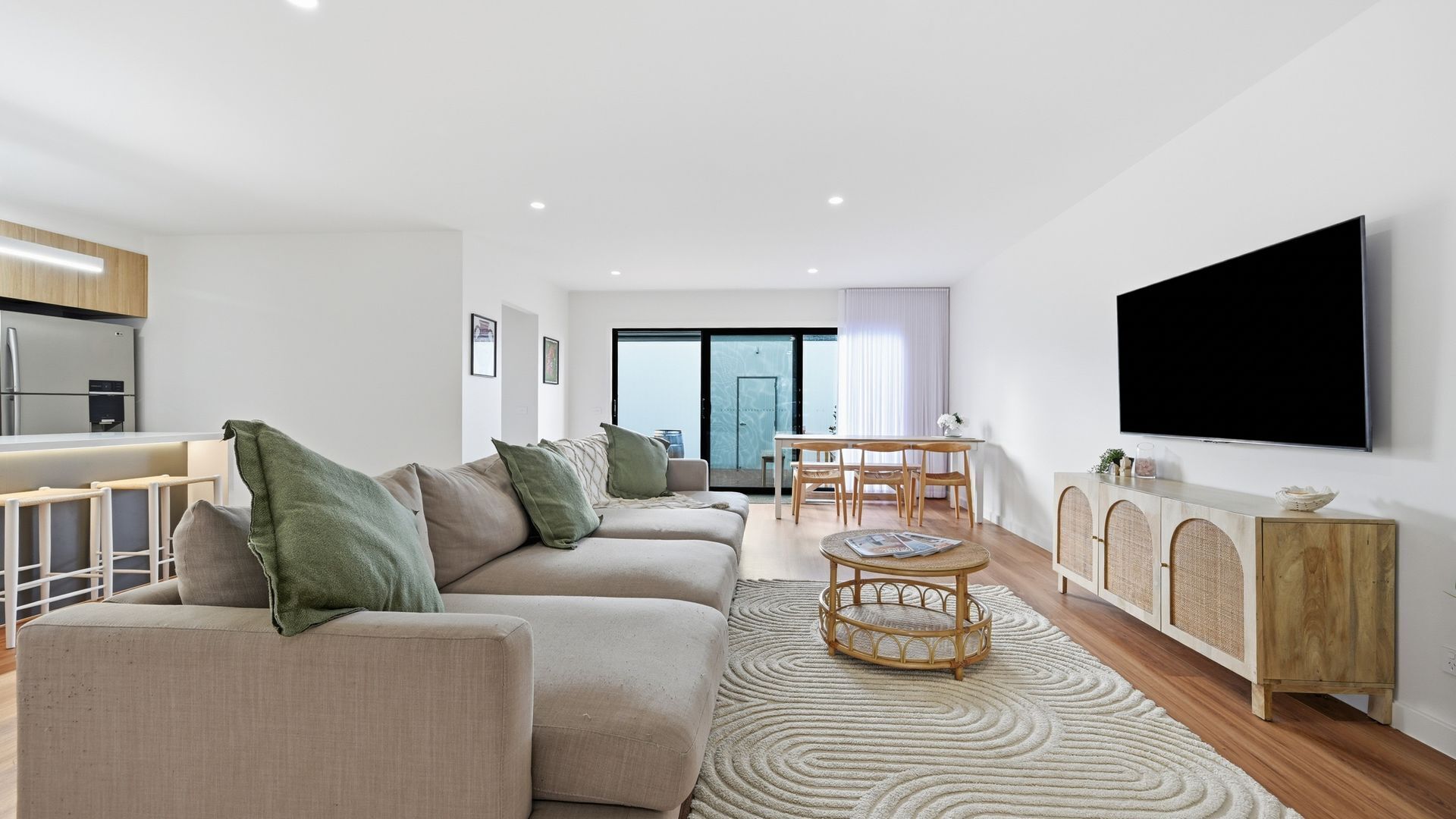Una sala de estar moderna con un conjunto de sofás, una mesa de comedor y un televisor de pantalla plana montado en la pared.