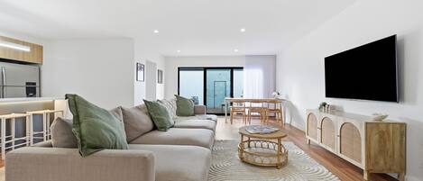 Una sala de estar moderna con un conjunto de sofás, una mesa de comedor y un televisor de pantalla plana montado en la pared.