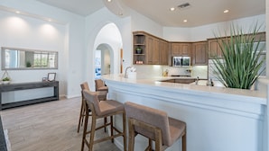 A modern kitchen with a central island, bar stools, wooden cabinets, and recessed ceiling lights.