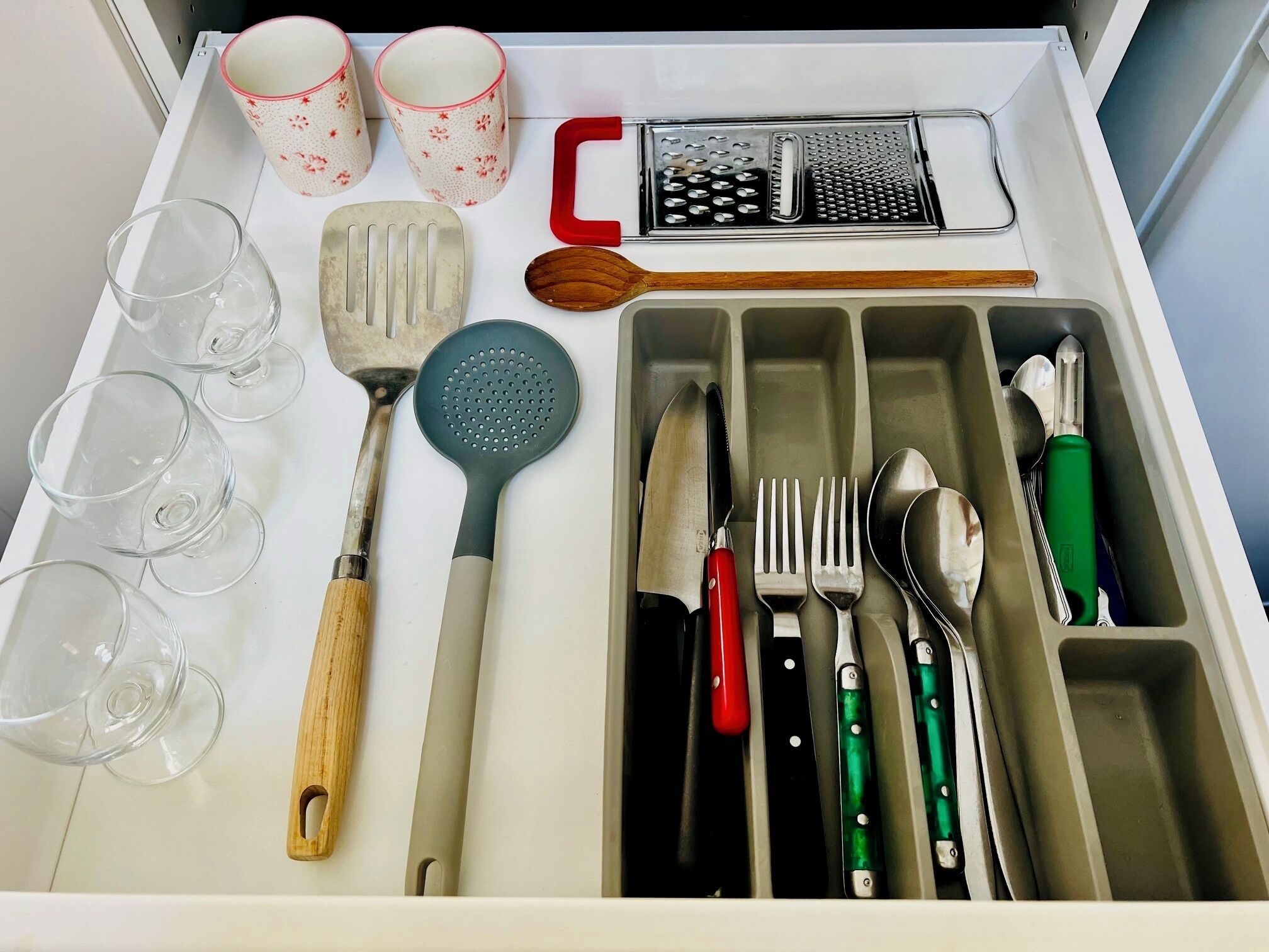 Un tiroir contenant des ustensiles de cuisine, notamment une râpe, une spatule et divers couteaux.
