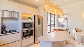 A modern kitchen with a built-in oven, microwave, and refrigerator. There is a round island with seating and a dining table with chairs. - Well-equipped Apartments 100m From the Beach - EVR (Porto Belo)
