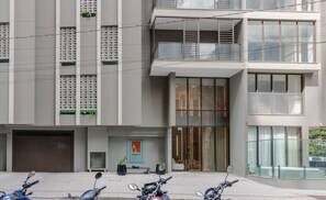 Un bâtiment moderne avec une entrée en verre, des plantes en pot et des scooters garés.