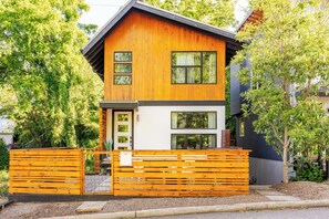 Una casa moderna de dos pisos con fachada de madera, ventanas grandes y valla frontal de madera.