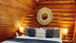 Ett mysigt sovrum inrett i stil med en timmerstuga, med en stor säng, två sänglampor och en vävd väggdekoration.
