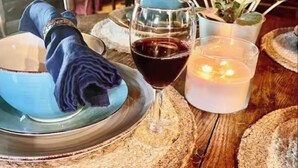 Ett matbord i trä med ett glas rött vin, ett ljus och en blå skål.