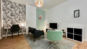 Ein modernes Wohnzimmer mit Holzboden, einem grünen Sofa, einem schwarzen Bürostuhl, einem Fernseher und einem Kamin.