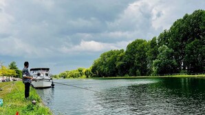 Ein ruhiger Fluss mit einem am linken Ufer vertäuten Boot, umgeben von üppigem Grün und Bäumen.