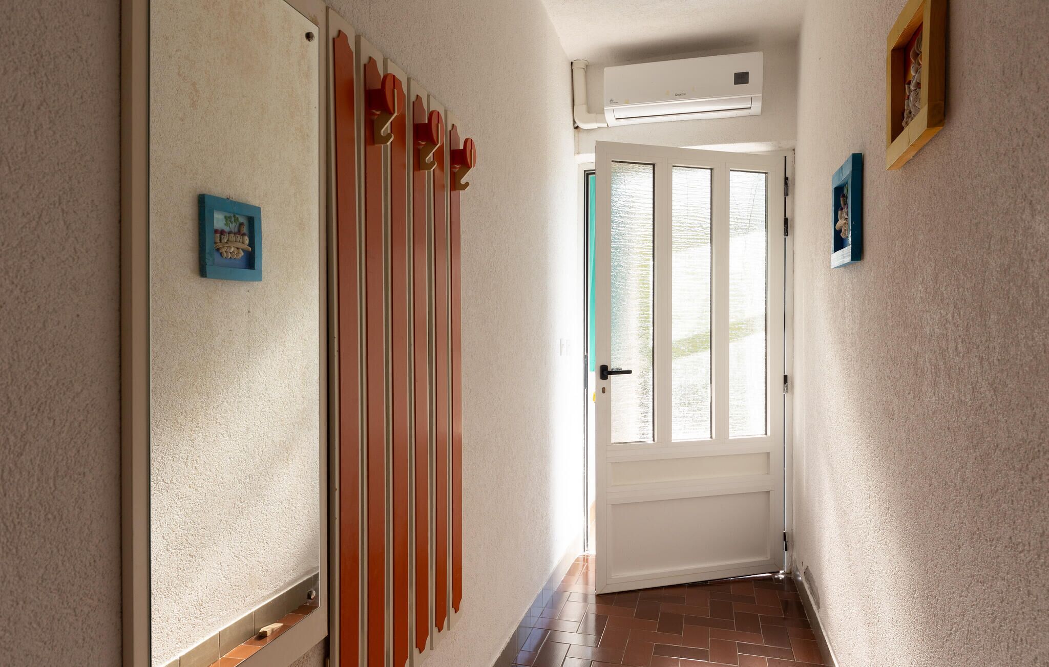 A hallway with a white door, a window with frosted glass, and a wall-mounted air conditioning unit.