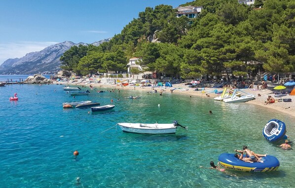 Una spiaggia con acque cristalline color turchese, barche e persone che nuotano.