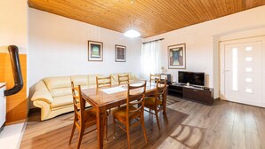 Un salon avec un plafond en bois, un canapé beige, une table à manger en bois avec des chaises, un téléviseur et des tableaux encadrés accrochés au mur.