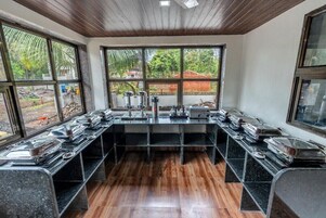 Una cocina con una encimera larga, varios electrodomésticos y grandes ventanales con vistas al exterior.