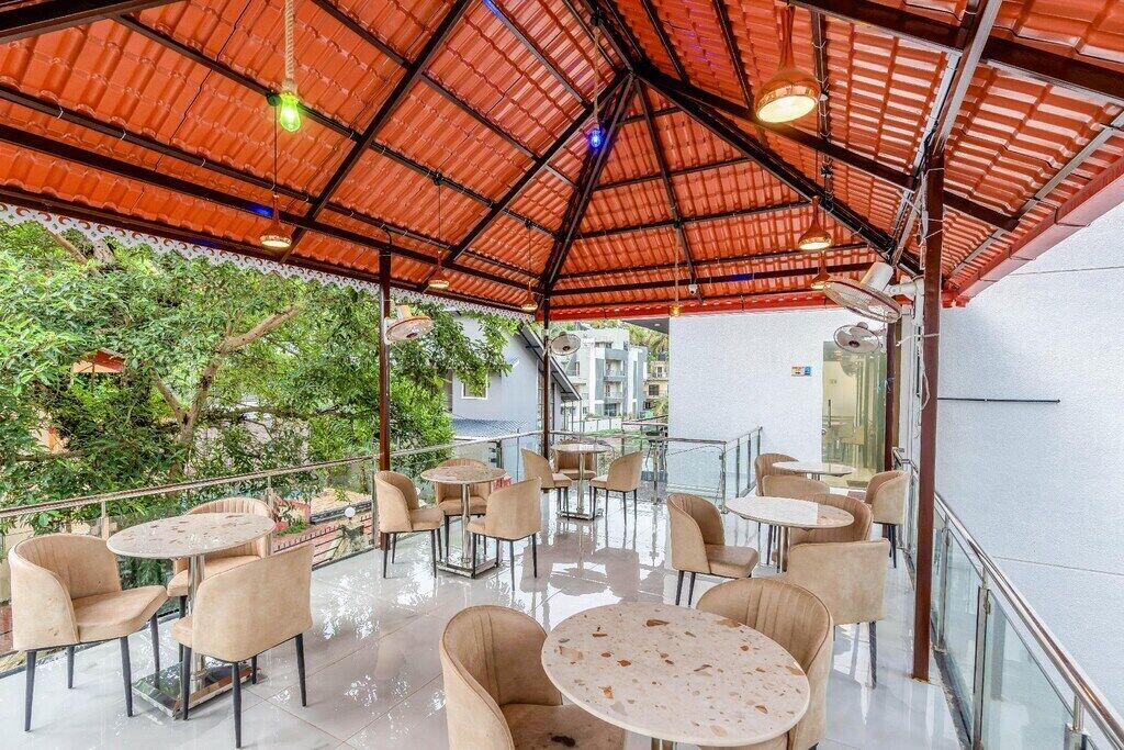 An outdoor café with round tables and chairs, a red metal roof, and a view of greenery.