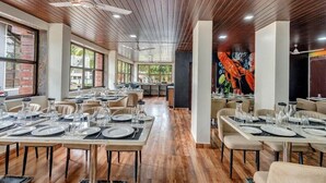 Restaurante com soalho de madeira, várias mesas de jantar postas com pratos e copos, e um ventilador de teto.