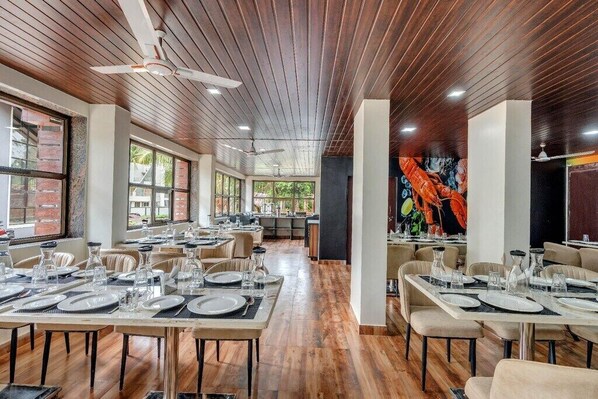 Un restaurant doté d’un plancher en bois, de plusieurs tables dressées avec des assiettes et des verres, et d’un ventilateur de plafond.