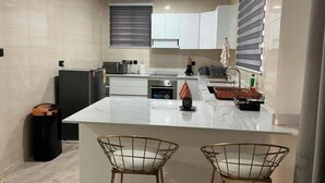 Une cuisine moderne avec des meubles blancs, un îlot central, deux chaises au design épuré et une poubelle.