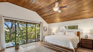 A bedroom with a large bed, wooden ceiling, and a view of trees through a sliding glass door. - Charming Coastal Retreat sleeps up to 9 (Fernandina Beach)