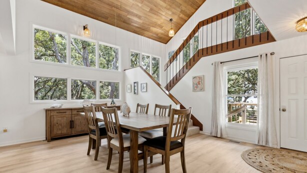 A dining area with a wooden table and chairs, a staircase, and large windows with a view of trees. - Charming Coastal Retreat sleeps up to 9 (Fernandina Beach)