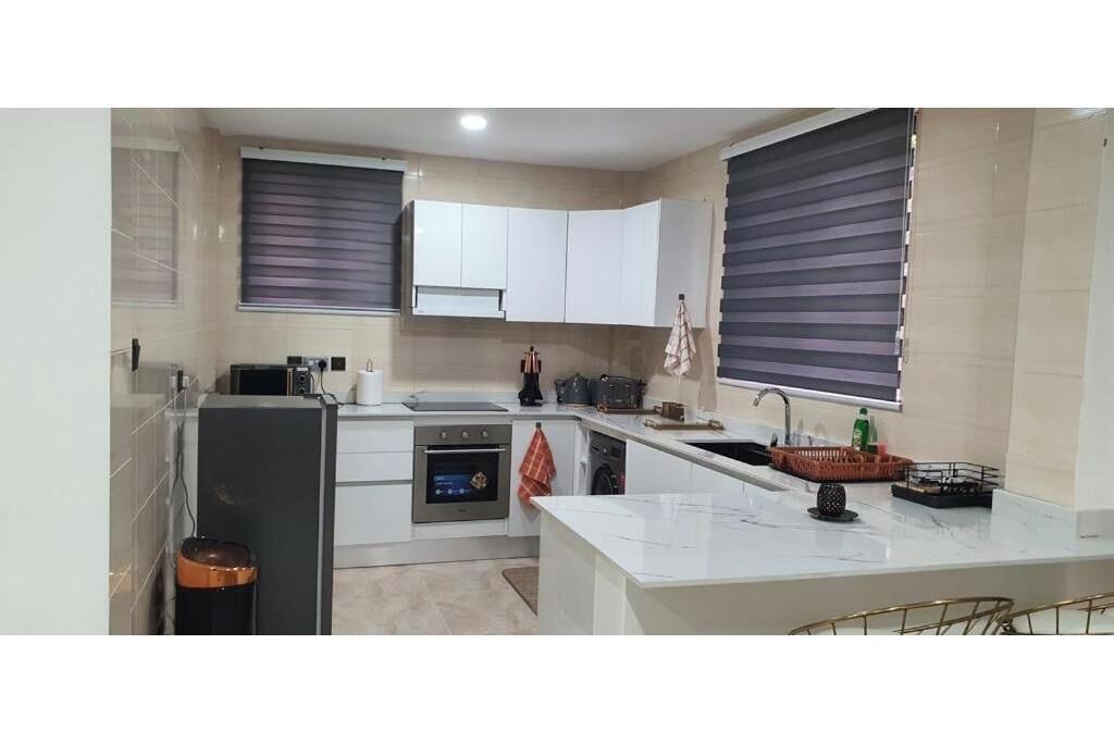 A modern kitchen with white cabinets, a built-in oven, a sink, and a window with blinds.