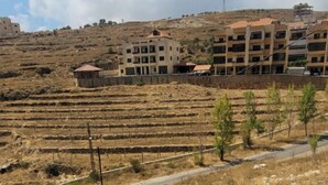 Blick auf eine Hügelsicht mit terrassierten Weinbergen und einem Gebäudekomplex im Hintergrund.