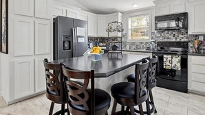 Une cuisine moderne avec des meubles blancs, un îlot central doté de chaises, un réfrigérateur, un four à micro-ondes et une cuisinière.