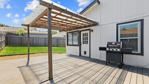 A covered patio with a grill area, a wooden deck, and a white building with a window and door. - Round Rock Retreat-3-bedroom house centrally located in Round Rock. W/Bonus room (Round Rock)