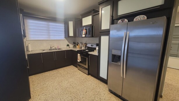 Una cocina con armarios oscuros, un refrigerador de acero inoxidable, una estufa y un lavamanos.