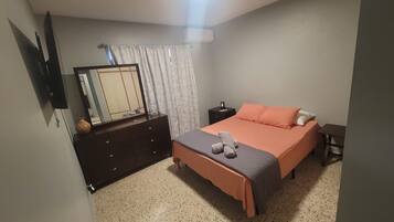 A bedroom with a bed, a dresser, a nightstand, a mirror, and a window with curtains.