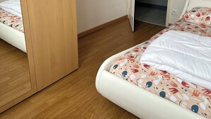 Een slaapkamer met een houten garderobe, een bed met een bedovertrek met patroon en een deur naar een andere kamer.
