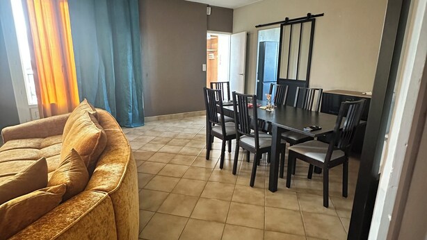 Een eethoek met een tafel, stoelen, een bank en een plafondlamp.