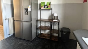 Een kleine keuken met een roestvrijstalen koelkast, een houten wandplank, een prullenbak en een aanrecht.
