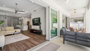 A spacious living room with a sofa, coffee table, and TV. There is a sliding glass door leading to a balcony with outdoor seating. - South Naples Pool House (Naples)