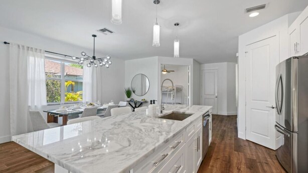 A modern kitchen with a large island, white cabinetry, and stainless steel appliances. - South Naples Pool House (Naples)