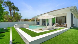 A modern outdoor pool area with a covered seating area and lounge chairs. - South Naples Pool House (Naples)