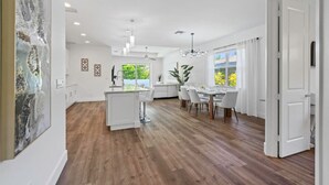 A spacious kitchen with a central island, a dining area with a large window, and a modern chandelier. - South Naples Pool House (Naples)