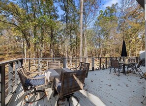 Une terrasse en bois, agrémentée de meubles en osier et d’une table, le tout entouré d’arbres.