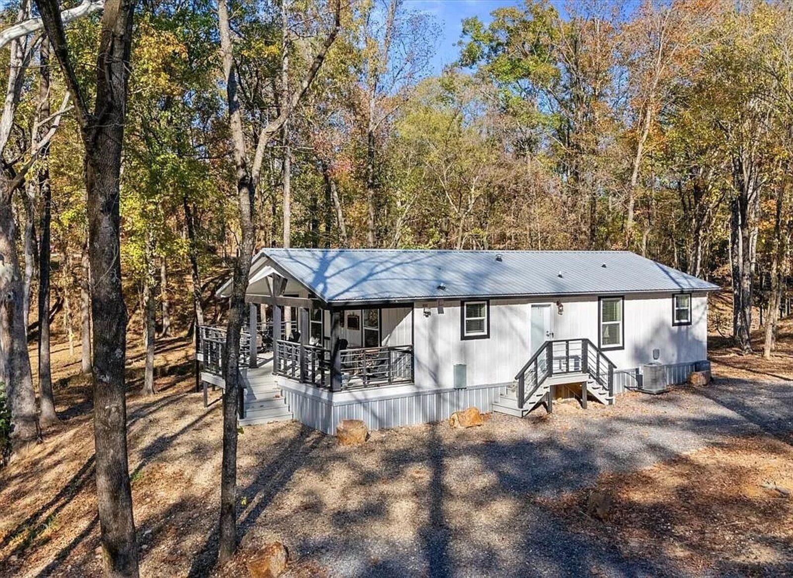 A single-story cabin with a covered porch, surrounded by trees.