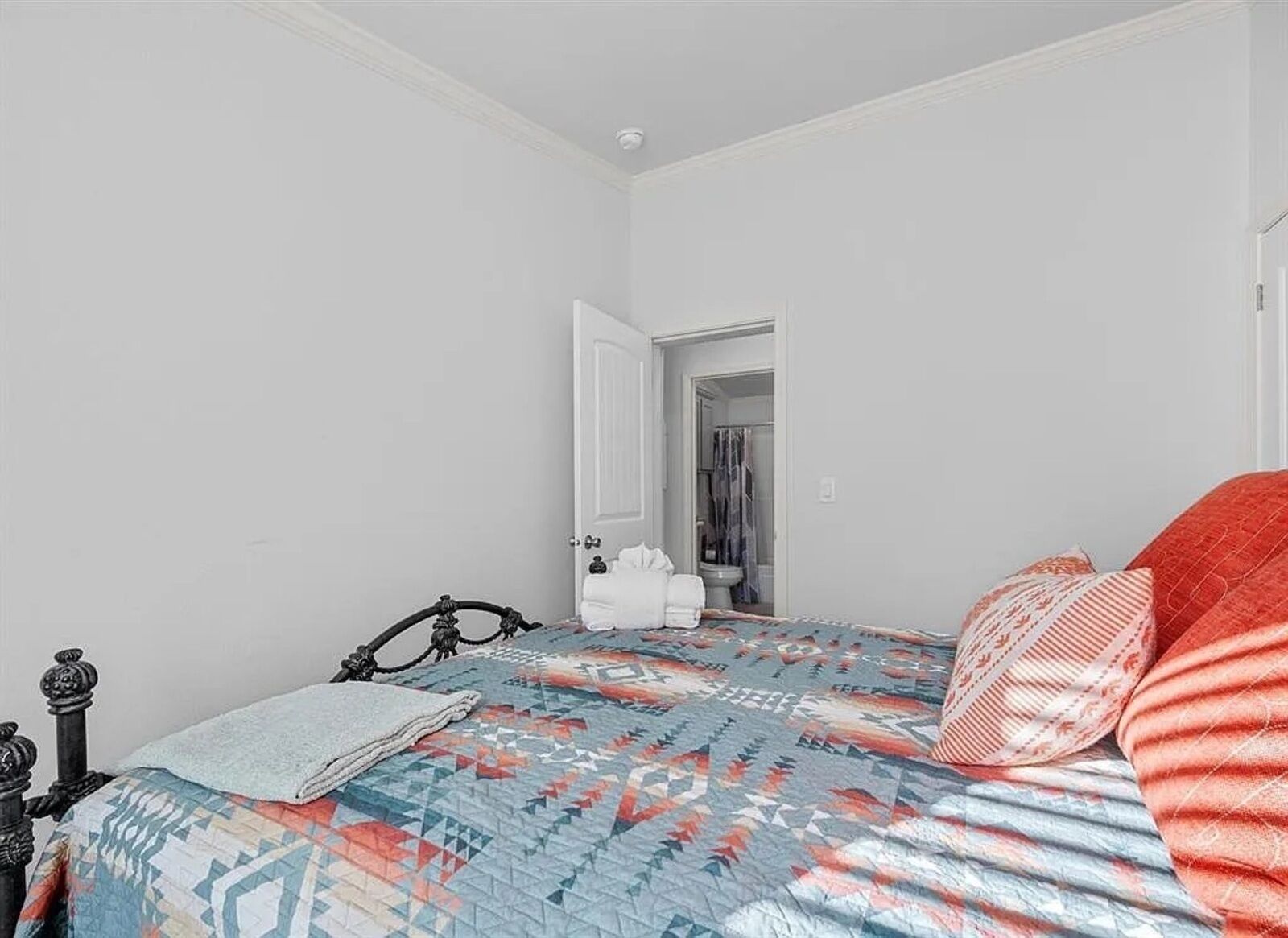 A bedroom with a bed, a door leading to a bathroom, and a white wall.