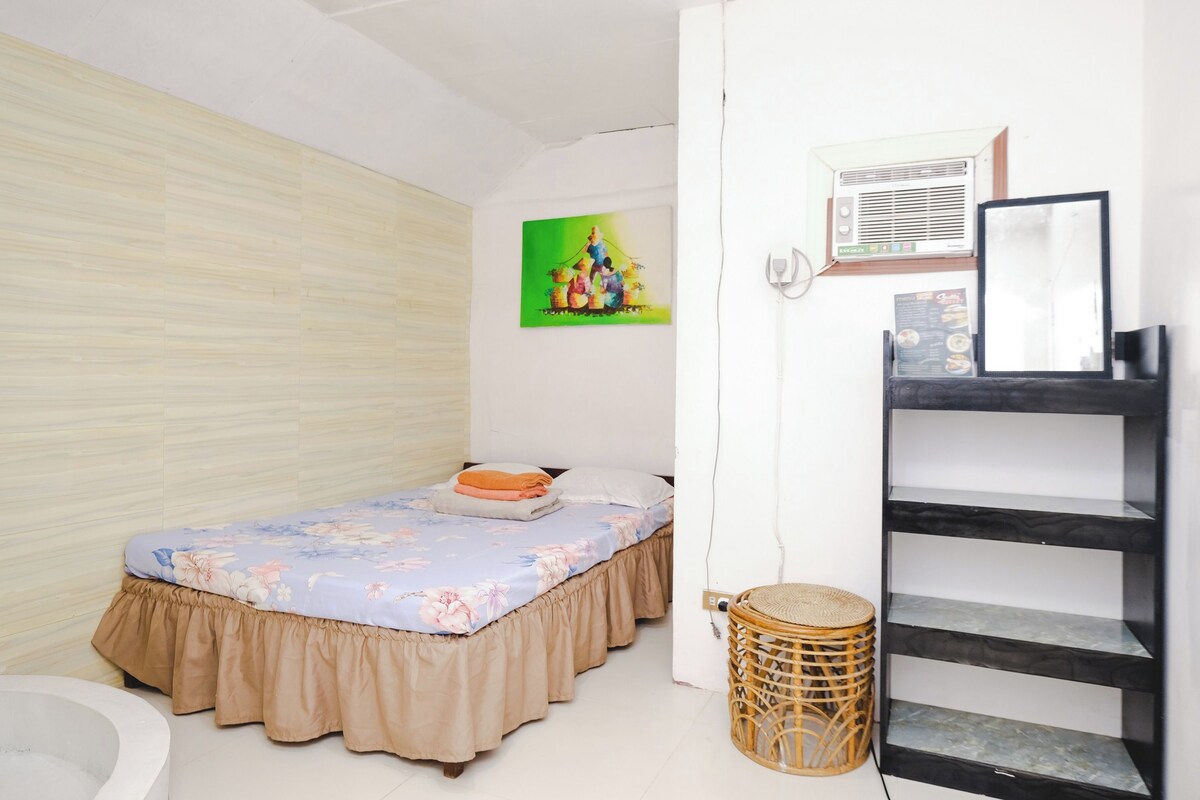 A bedroom with a bed, a wall-mounted air conditioner, a painting, and a small wicker basket.