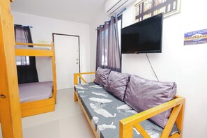A room with bunk beds, a sofa, a flat-screen TV, and a sign about surf lessons. - Monaliza Surf Resort By Zuzu (San Juan)
