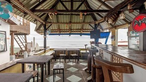 A covered outdoor seating area with tables and chairs, overlooking the sea. - Monaliza Surf Resort By Zuzu (San Juan)
