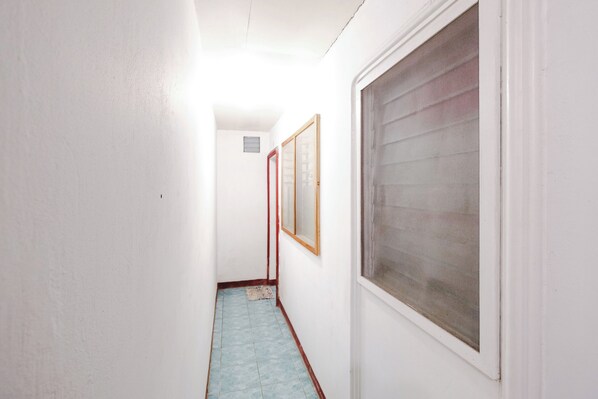 A narrow hallway with a window on the right, a door at the end, and a vent on the wall. - Monaliza Surf Resort By Zuzu (San Juan)