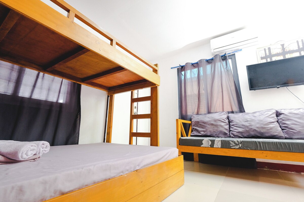 A room with a bunk bed, a sofa bed, a TV, and a window with curtains.